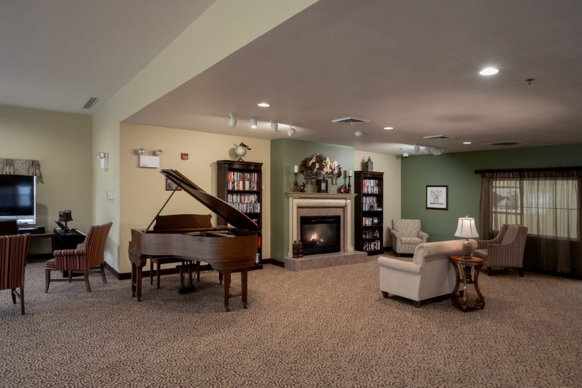 A cozy living room featuring a grand piano, comfortable seating, and a fireplace surrounded by bookshelves.