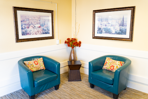 A cozy seating area featuring two teal armchairs with decorative pillows, a small table, and floral arrangements, complemented by framed artwork on the walls.