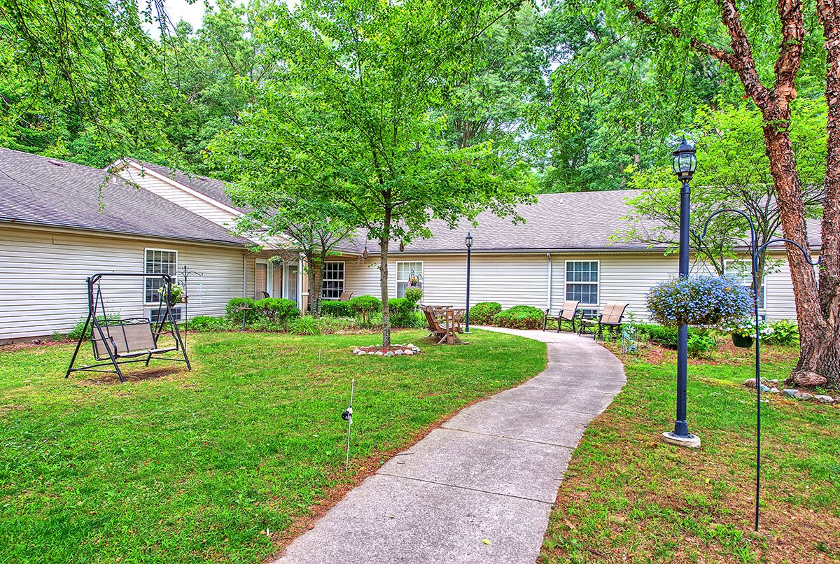 A peaceful garden with a pathway leading to a house surrounded by trees.