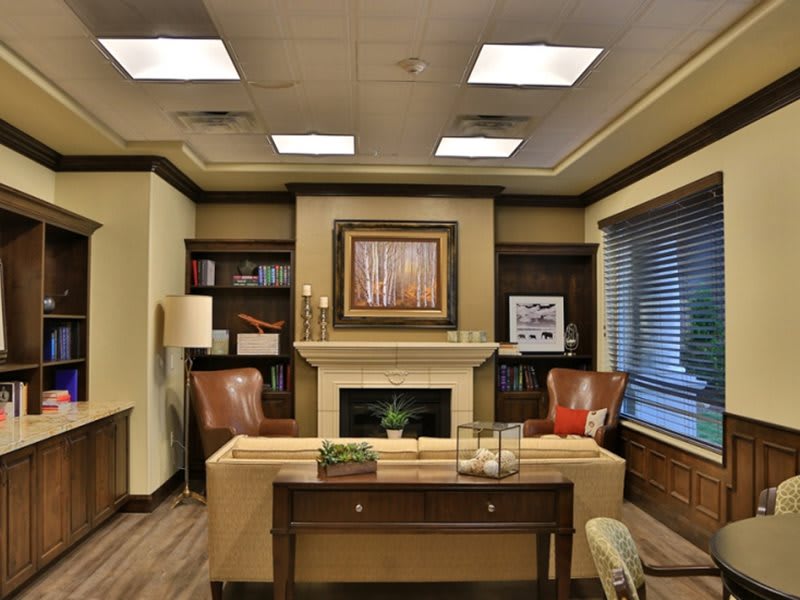 A well-appointed office space featuring a central desk, flanked by bookshelves and comfortable chairs with artwork above the fireplace.