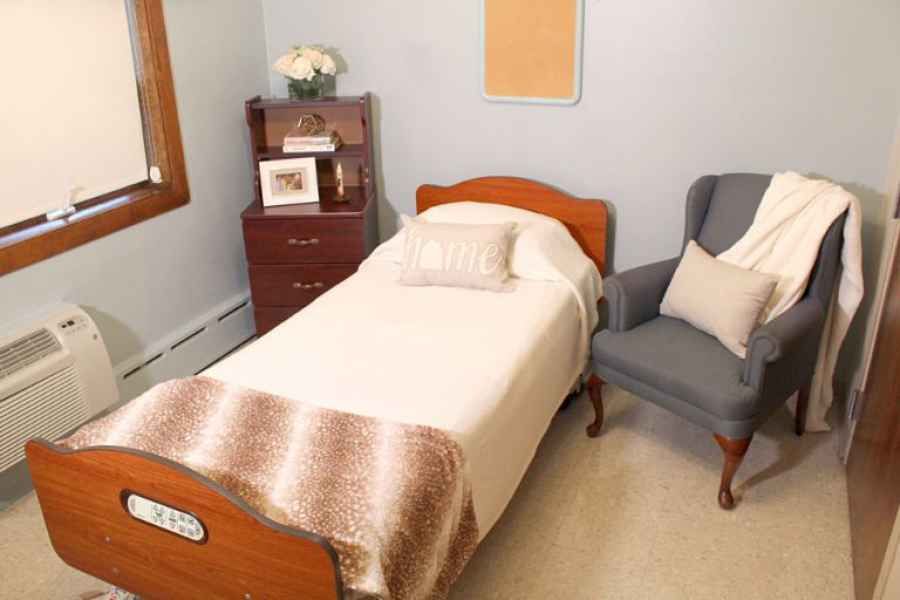 A cozy bedroom featuring a quaint single bed, an upholstered chair, and a wooden nightstand with decorative elements.