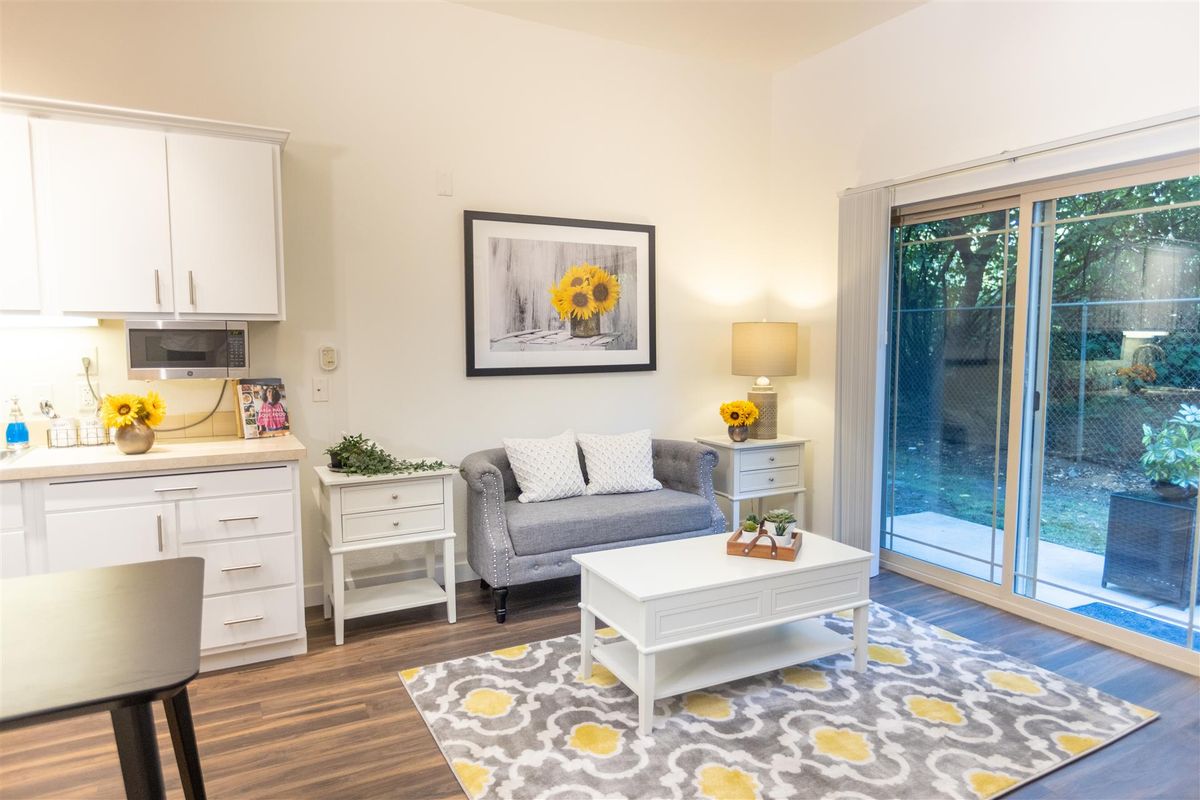 A cozy and modern living room featuring a gray sofa, white coffee table, patterned rug, and bright wall art.