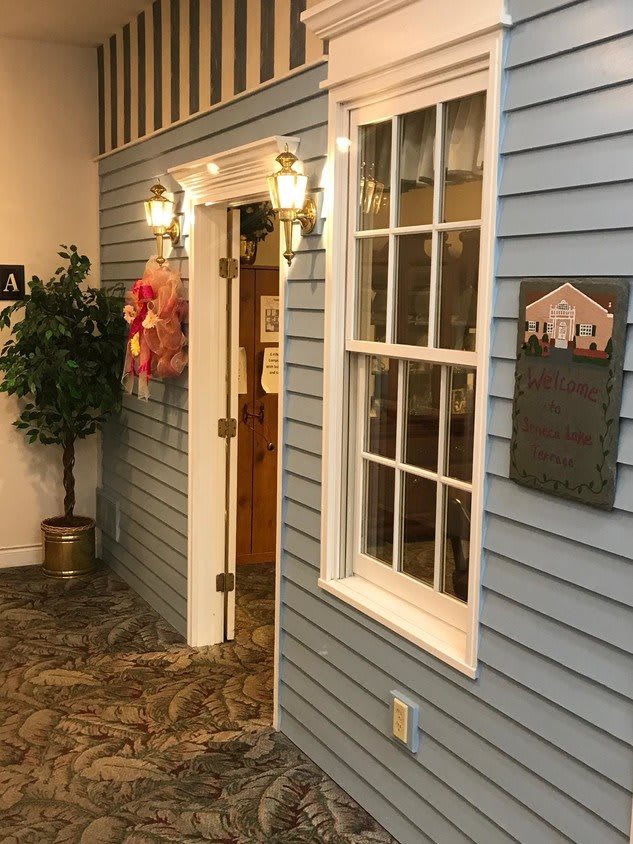 A cozy interior space designed to resemble the exterior of a house, featuring a doorway, large window, and decorative elements like an artificial plant and lamps.