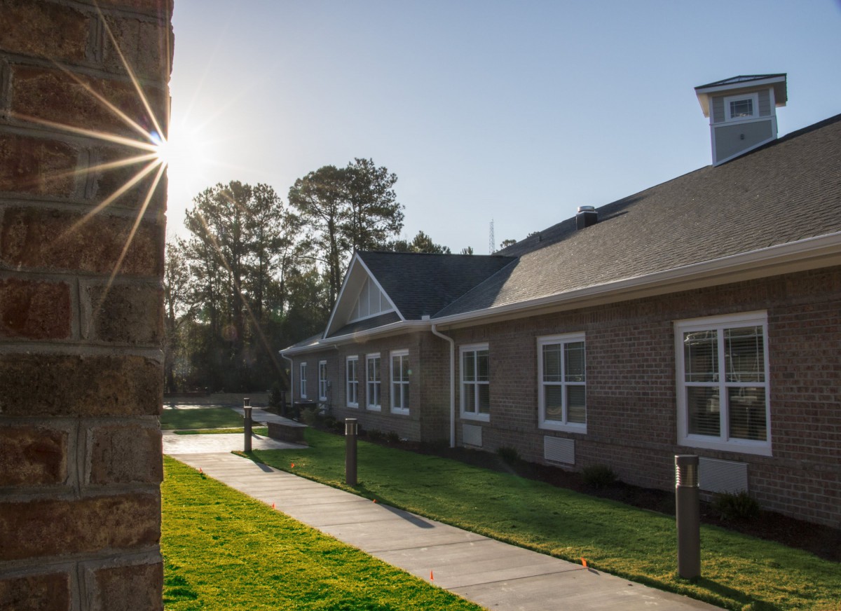 A building with a brick exterior illuminated by bright sunlight, surrounded by a green lawn and trees.