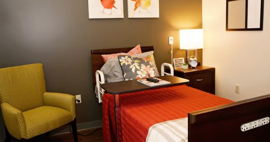 A well-appointed hospital room with a cozy bed, colorful pillows, and a bedside table equipped with a lamp.
