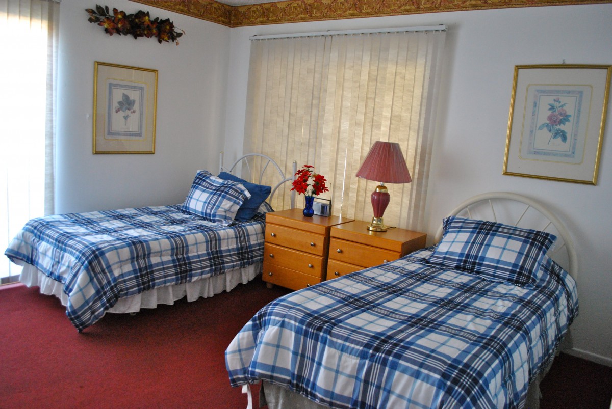 A cozy bedroom with two twin beds featuring plaid bedding, a dresser, and a lamp by the window.