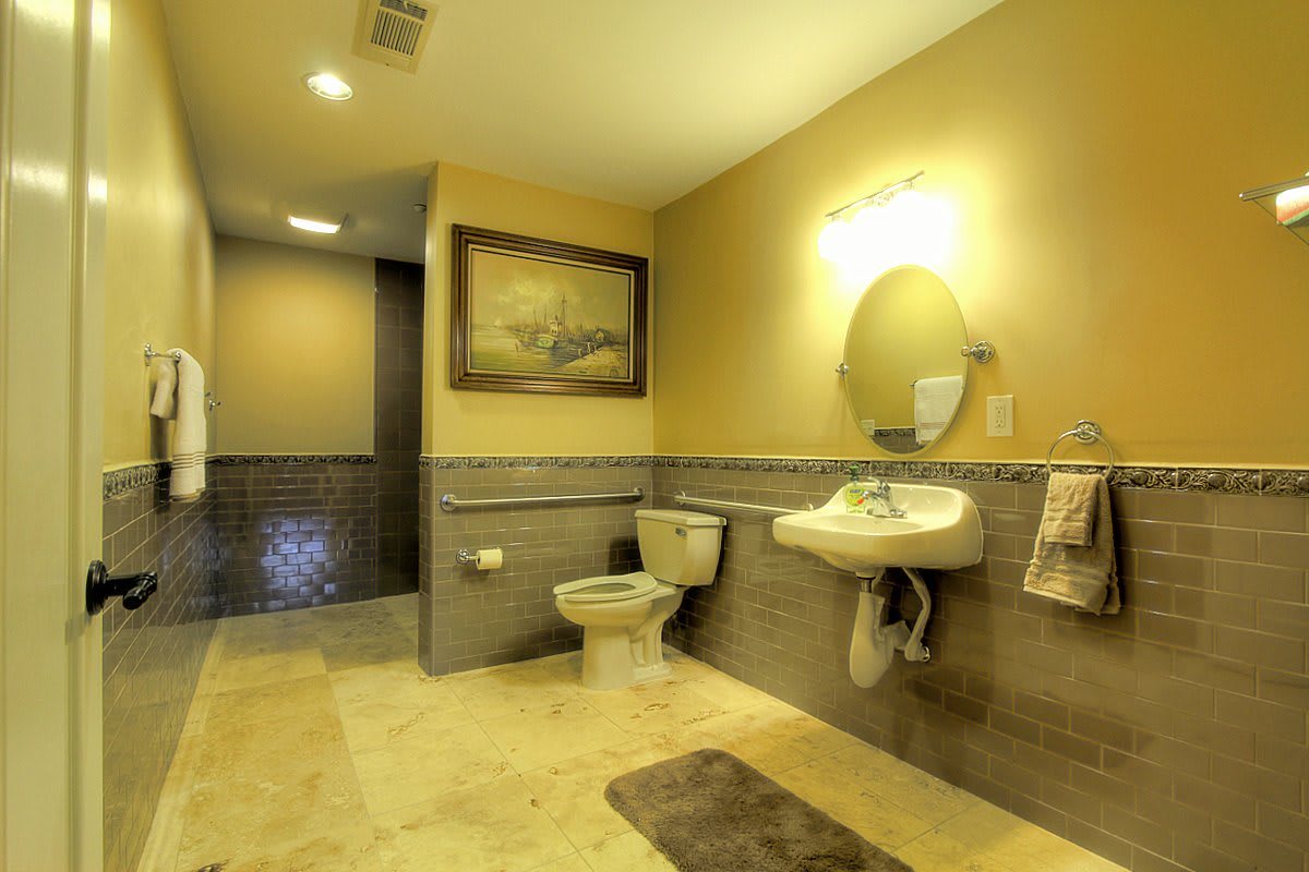 A spacious and well-lit bathroom featuring a sink, toilet, mirror, and decorative wall art.