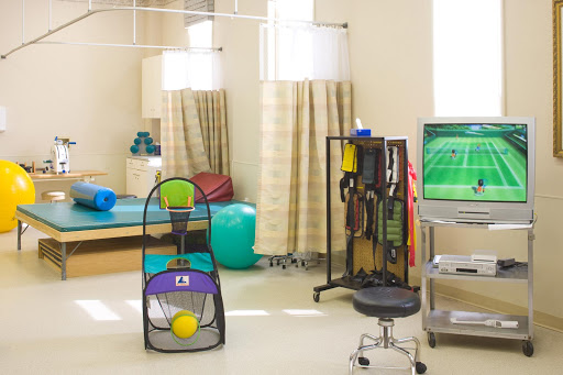 A therapy room equipped with various exercise and rehabilitation tools, including colorful balls and a monitor for treatment guidance.