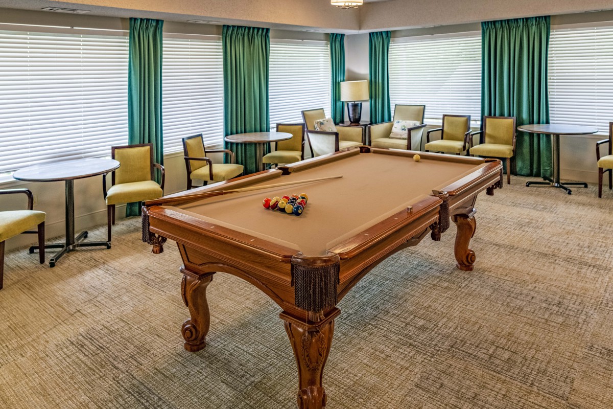 A cozy game room featuring a billiard table surrounded by comfortable seating and elegant curtains.