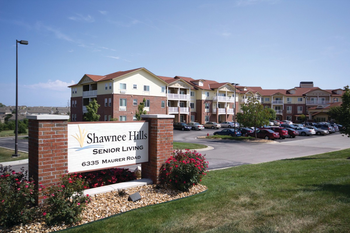 A large residential building with a sign reading 'Shawnee Hills Senior Living' and a parking lot in the foreground.