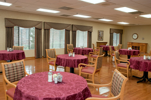 A spacious dining area featuring tables with red tablecloths and comfortable chairs, illuminated by natural light from large windows.