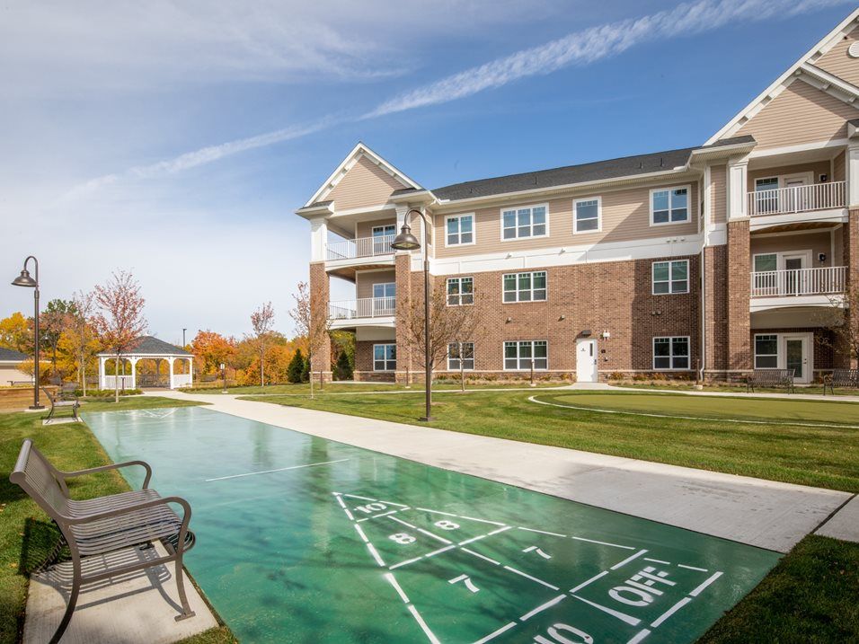 A modern apartment complex with an outdoor shuffleboard court and well-maintained green lawn under a clear blue sky.