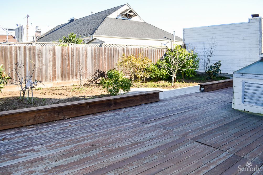 A backyard featuring a wooden deck and garden area, enclosed by a wooden fence.