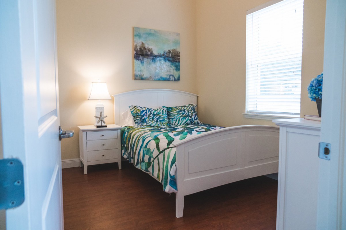 A cozy bedroom with a white bed frame, colorful bedding, and a nightstand with a lamp.