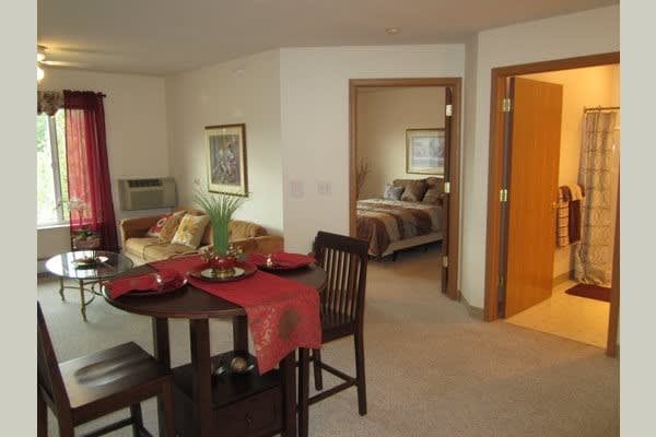 A cozy apartment interior featuring a living room with a dining area and an adjoining bedroom.