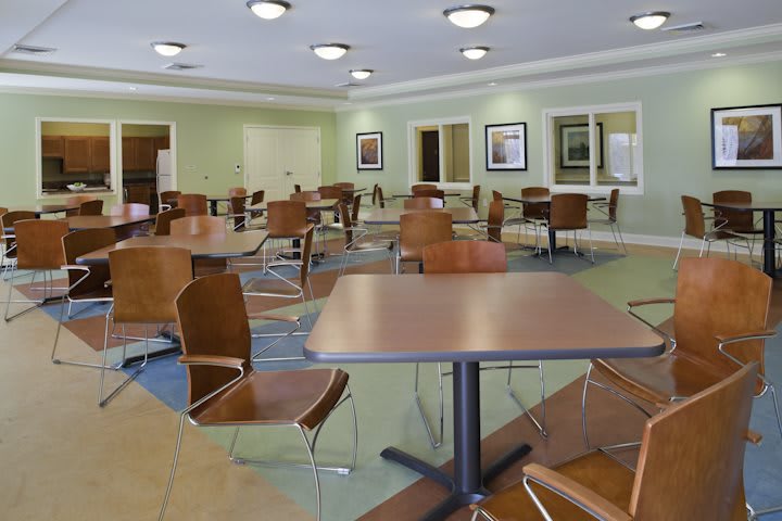 An empty cafeteria with modern tables and chairs, softly lit with ceiling lights.