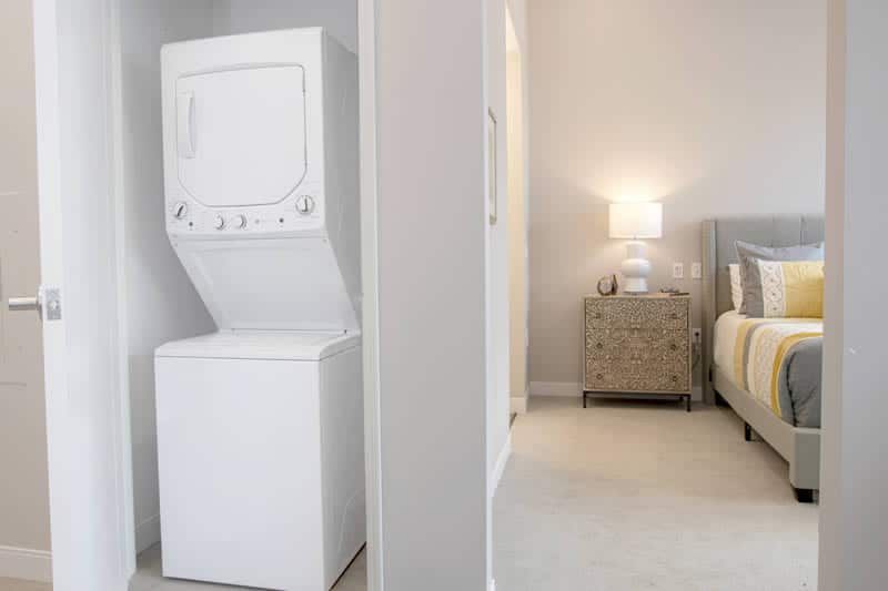 A compact laundry area with a stacked washer and dryer next to a cozy bedroom.
