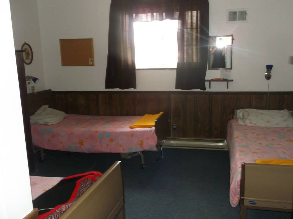 A simple room with two single beds, a window with curtains, and a mirror on the wall.
