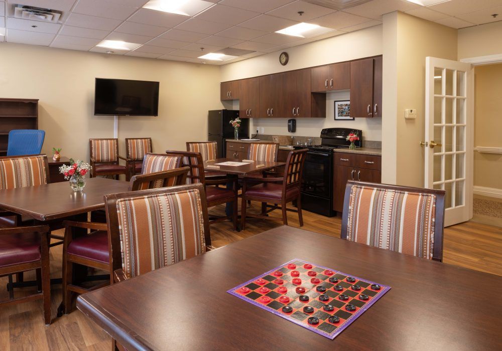 A cozy common area with a kitchenette, tables with seating, and a checkers board ready for play.