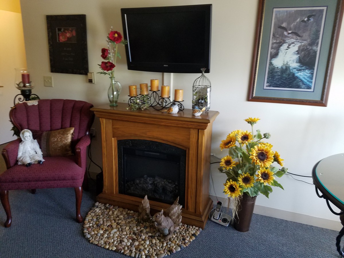 A cozy living room with a decorative fireplace, sunflowers, and artwork on the wall.