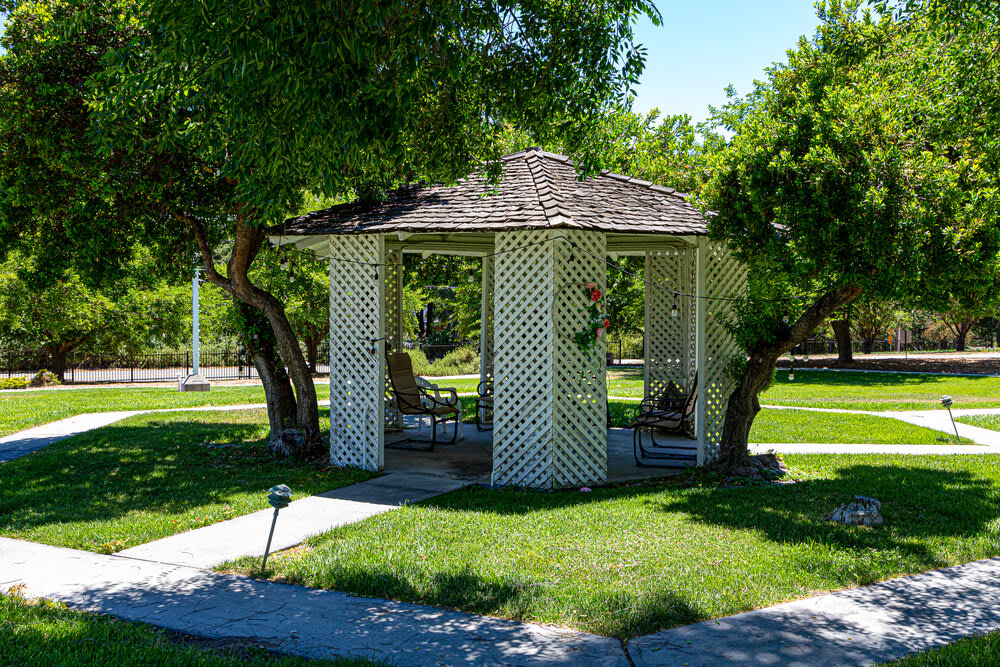A charming lattice gazebo surrounded by greenery in a sunny park setting.