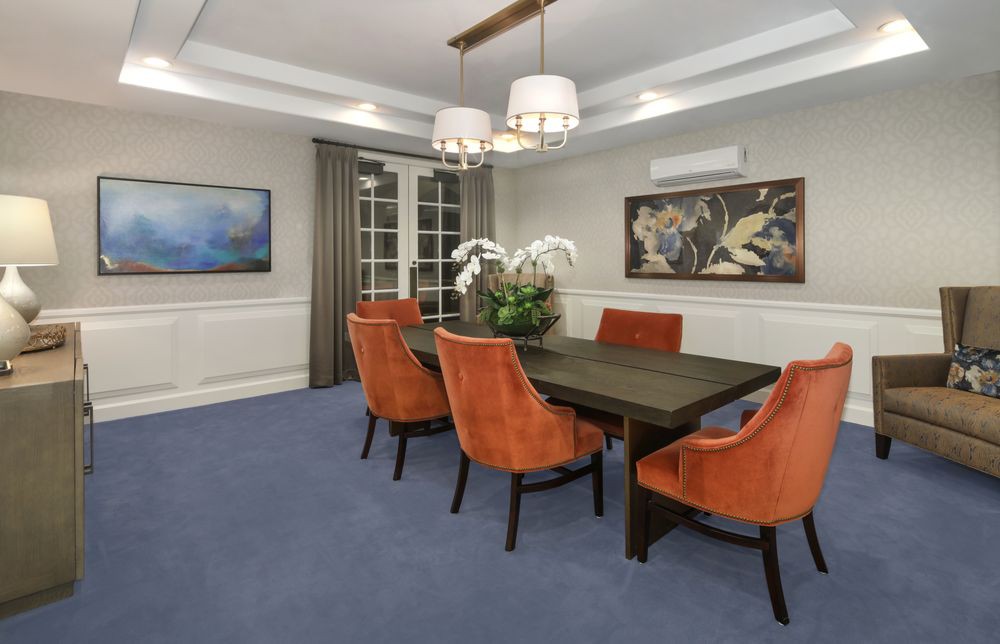 A modern dining room featuring orange chairs around a dark table, adorned with a central plant and illuminated by elegant chandeliers.