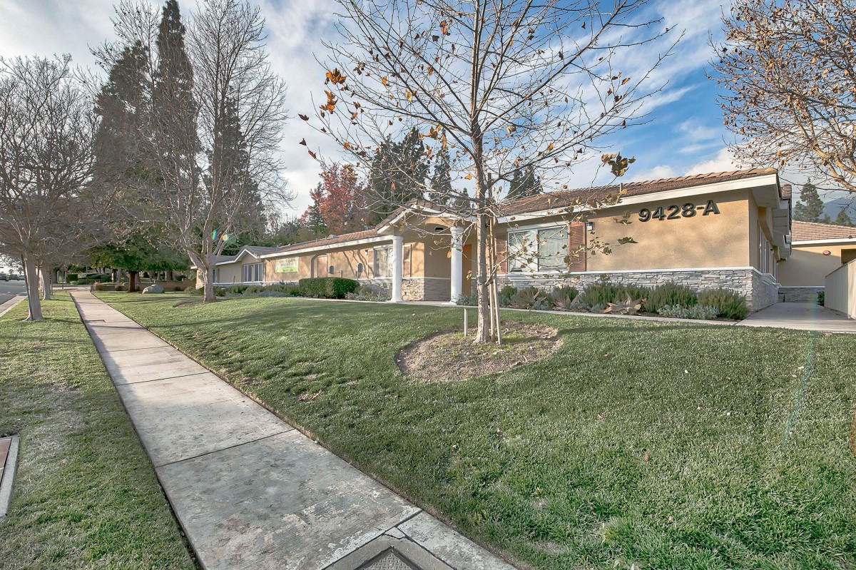 A suburban house with a manicured lawn and surrounding trees on a bright day.