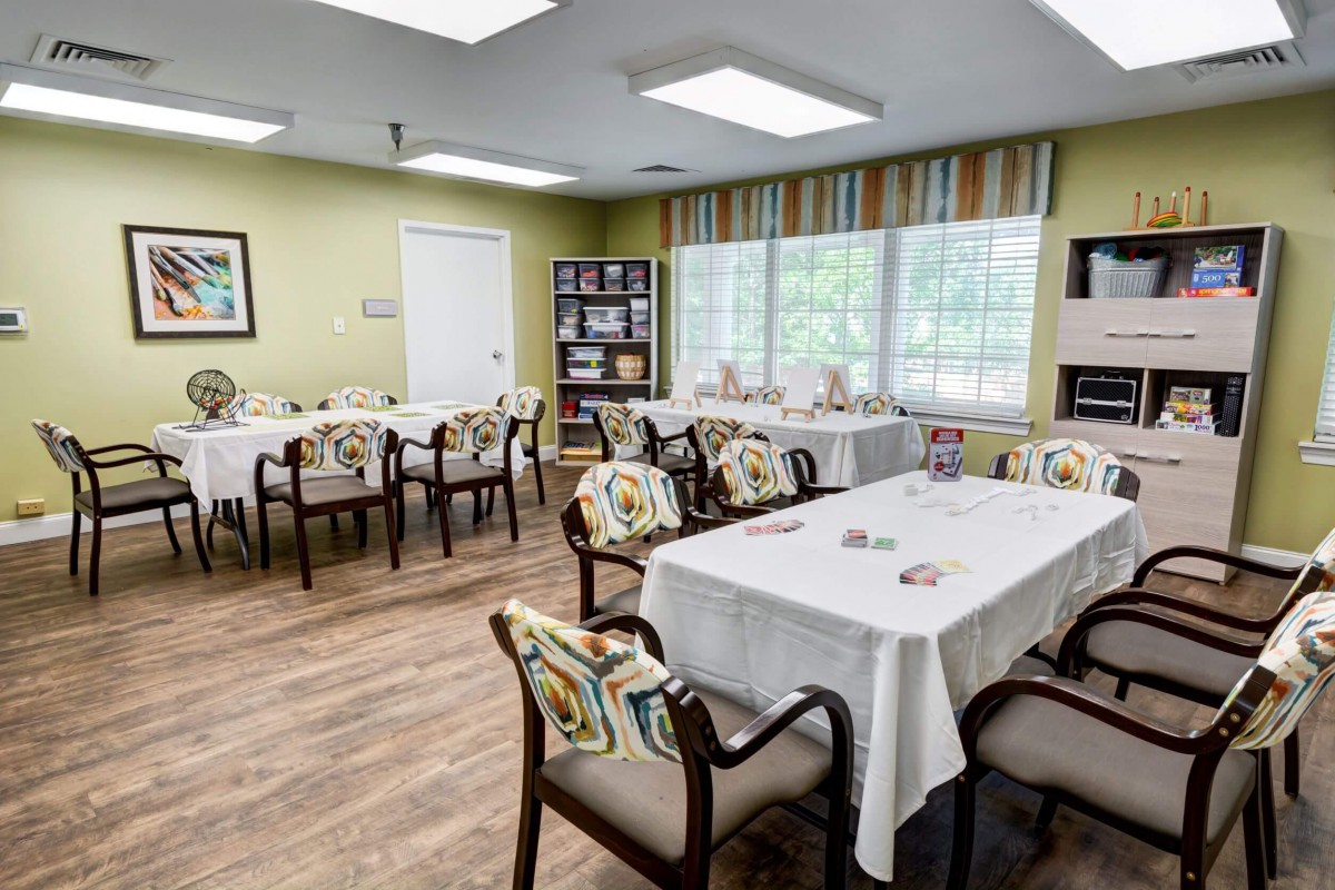 A well-lit dining room with tables and chairs, decorated with curtains and natural light coming through the windows.
