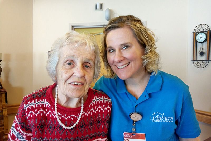 An elderly woman and her caregiver smiling together indoors.