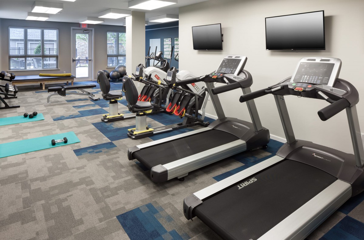 A modern gym featuring treadmills and elliptical machines, equipped with wall-mounted televisions.