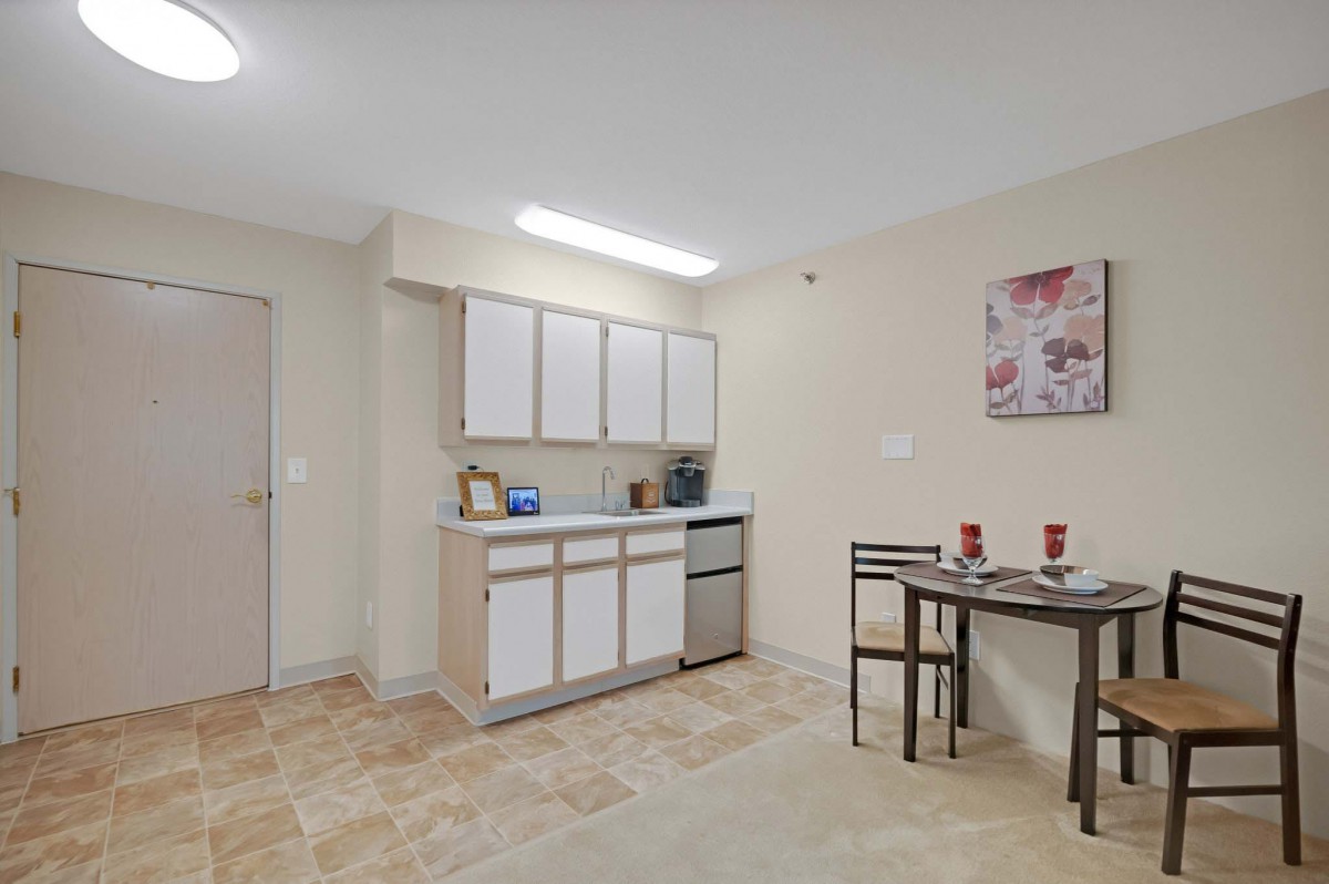 A compact kitchen and dining area featuring white cabinets and a small table set in a minimalist design.