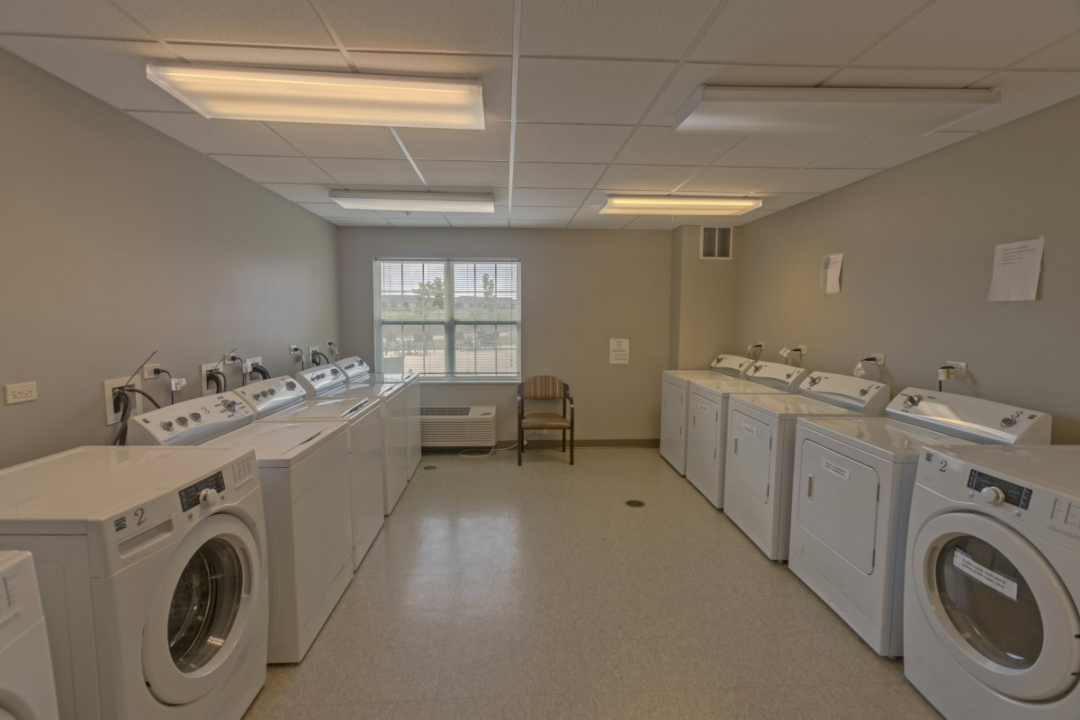 A laundry room with multiple washing machines and dryers lined up along the walls.
