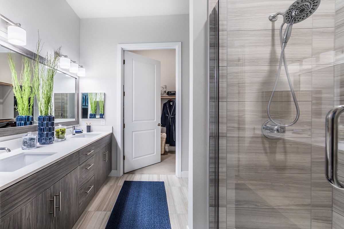 A modern bathroom with a sleek shower, double sink vanity, and a blue rug.