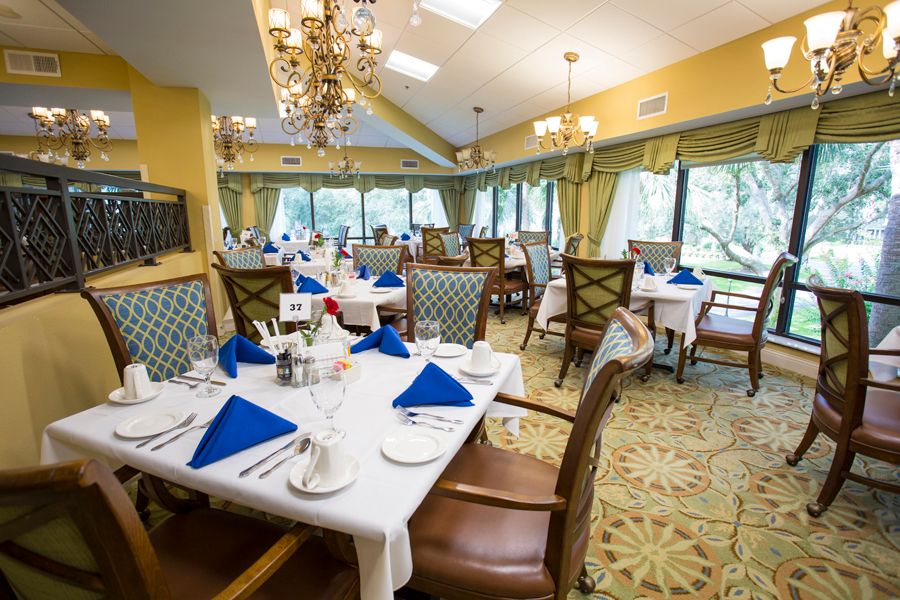 An elegant dining room with neatly arranged tables, featuring blue napkins and chandeliers.