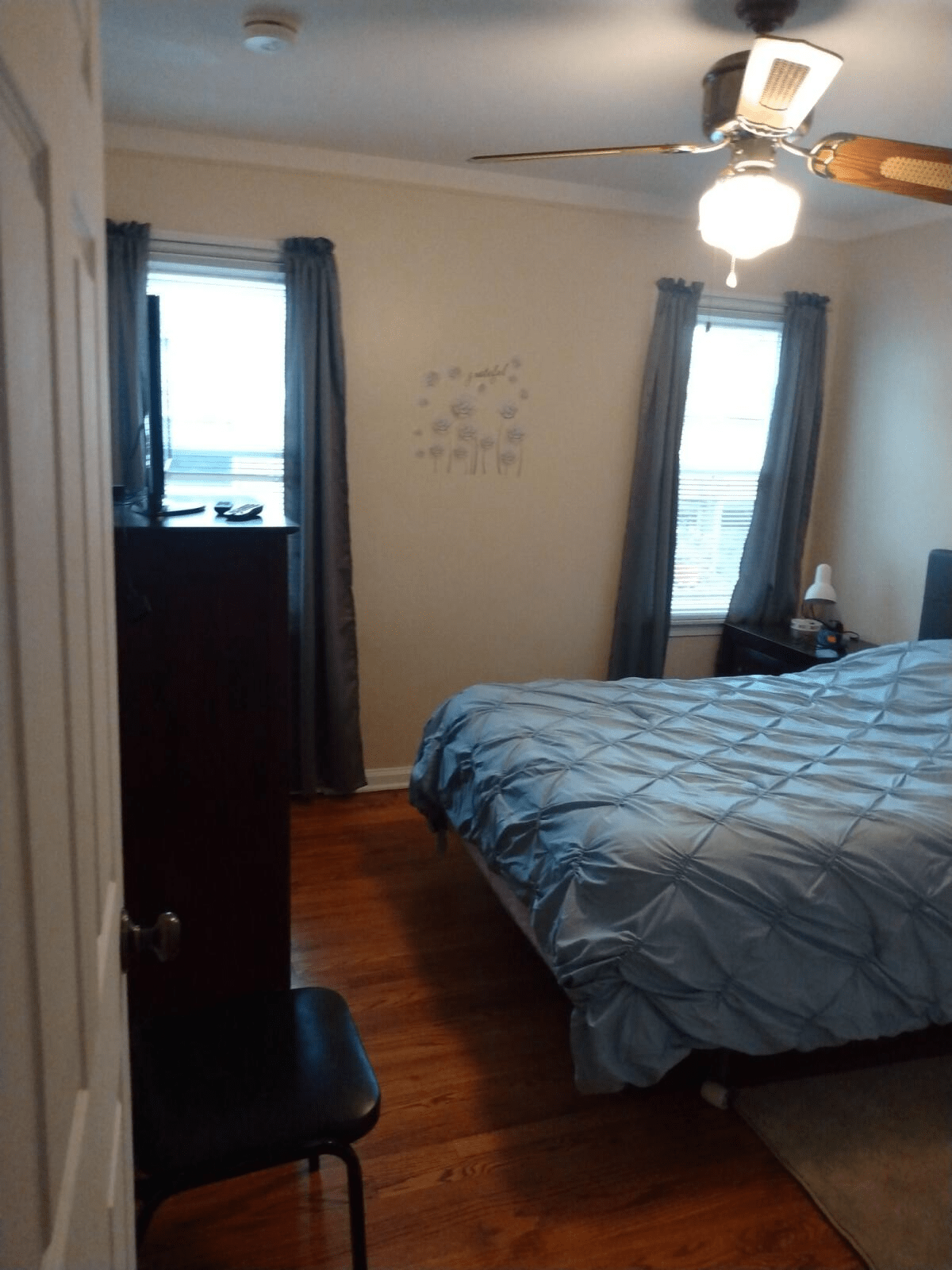 A cozy bedroom with a neatly made bed, curtains on the windows, and wooden furniture.