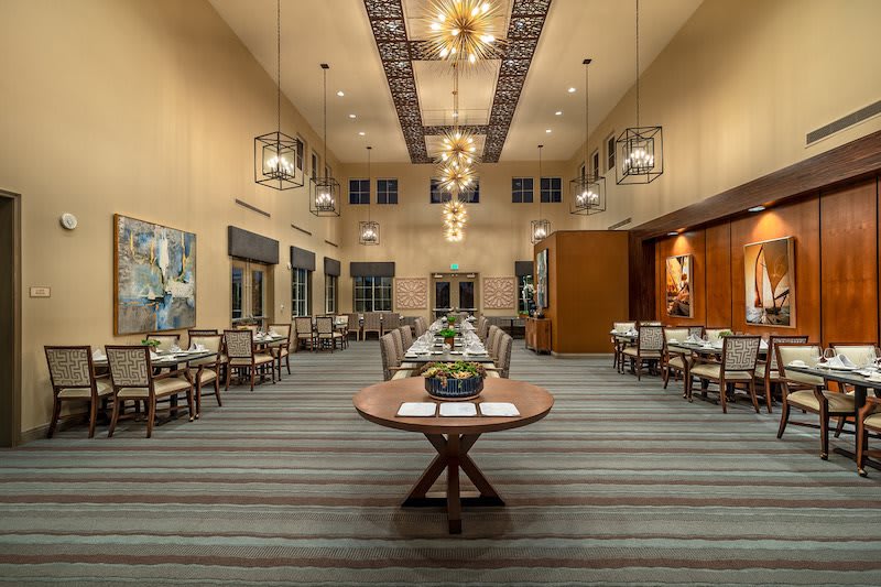 A spacious and elegantly designed dining room with tables and chairs arranged neatly under ornate chandeliers.