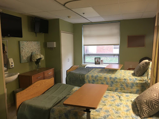 A view of a hospital patient room equipped with two beds, a television, and a window.