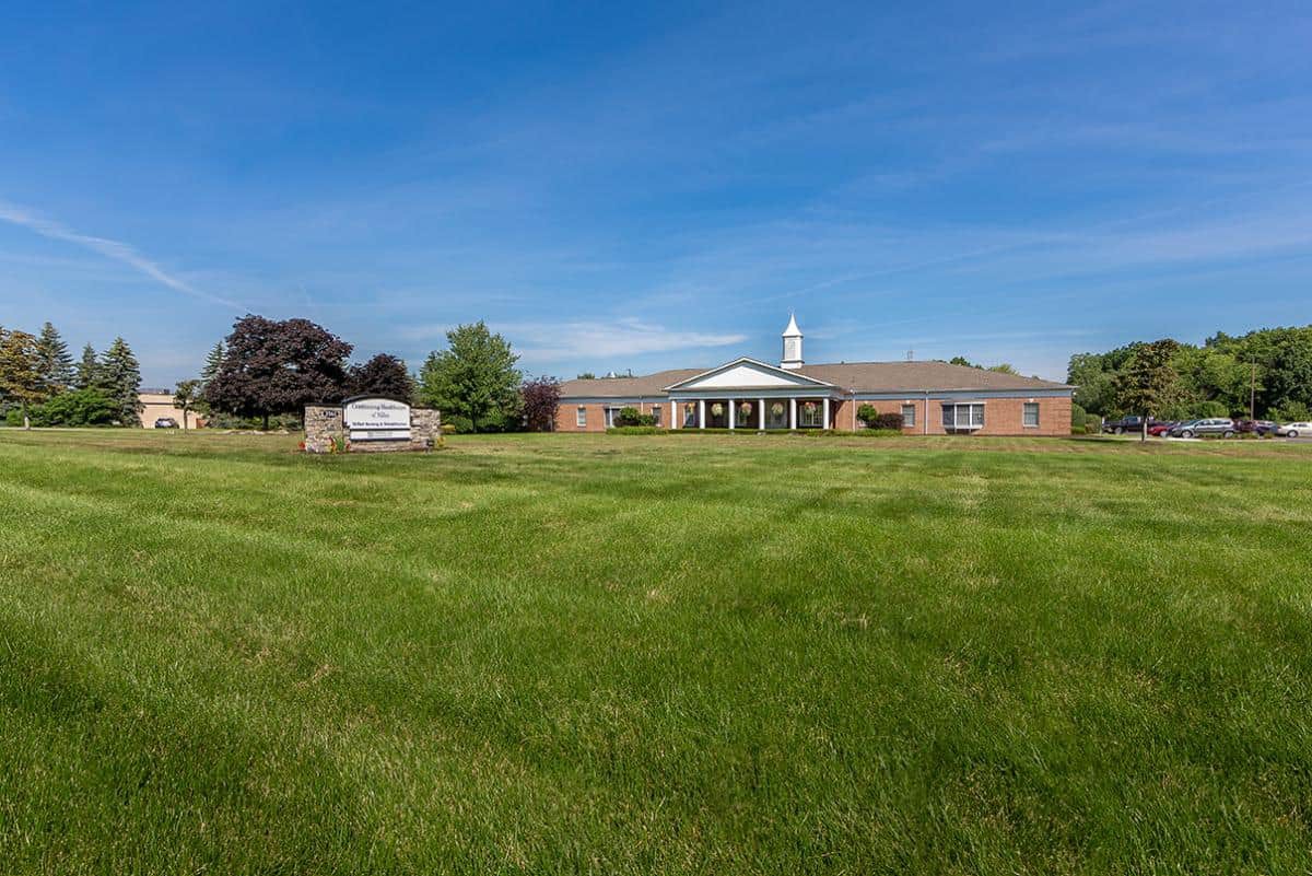 A wide lawn stretches out in front of a brick church under a blue sky.