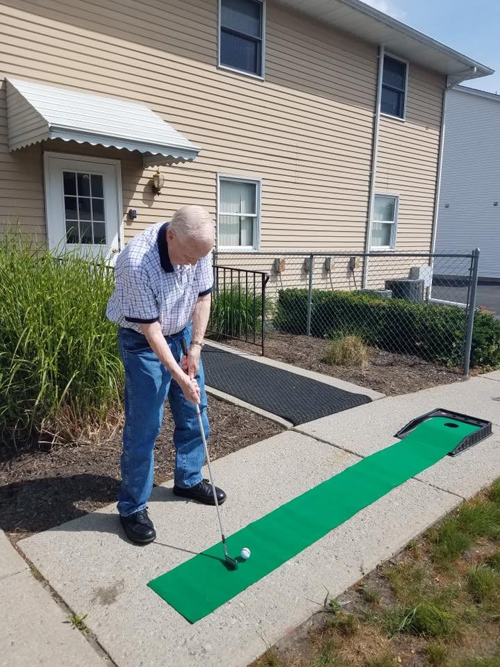 A person playing mini golf outdoors on a green mat.