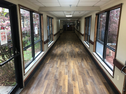 A well-lit corridor featuring windows on either side and a wooden floor, creating an inviting atmosphere.