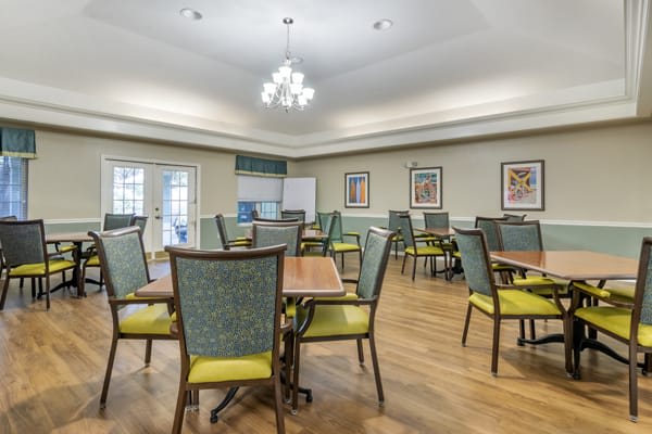 A well-lit dining area with multiple tables and chairs arranged neatly under a chandelier.
