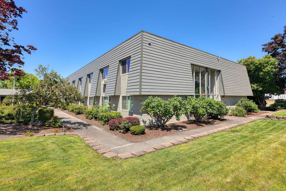 A modern commercial building with well-maintained landscaping and a clear blue sky.