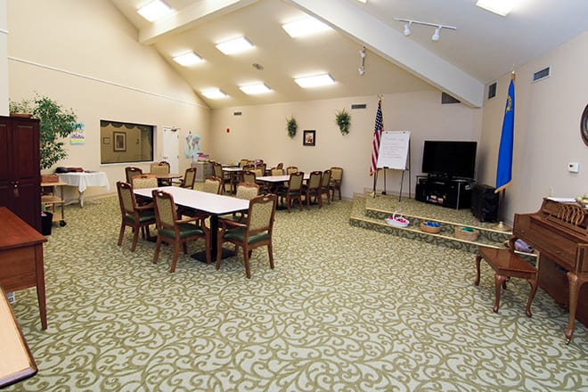 A community meeting room with tables, chairs, a television, and an American flag.