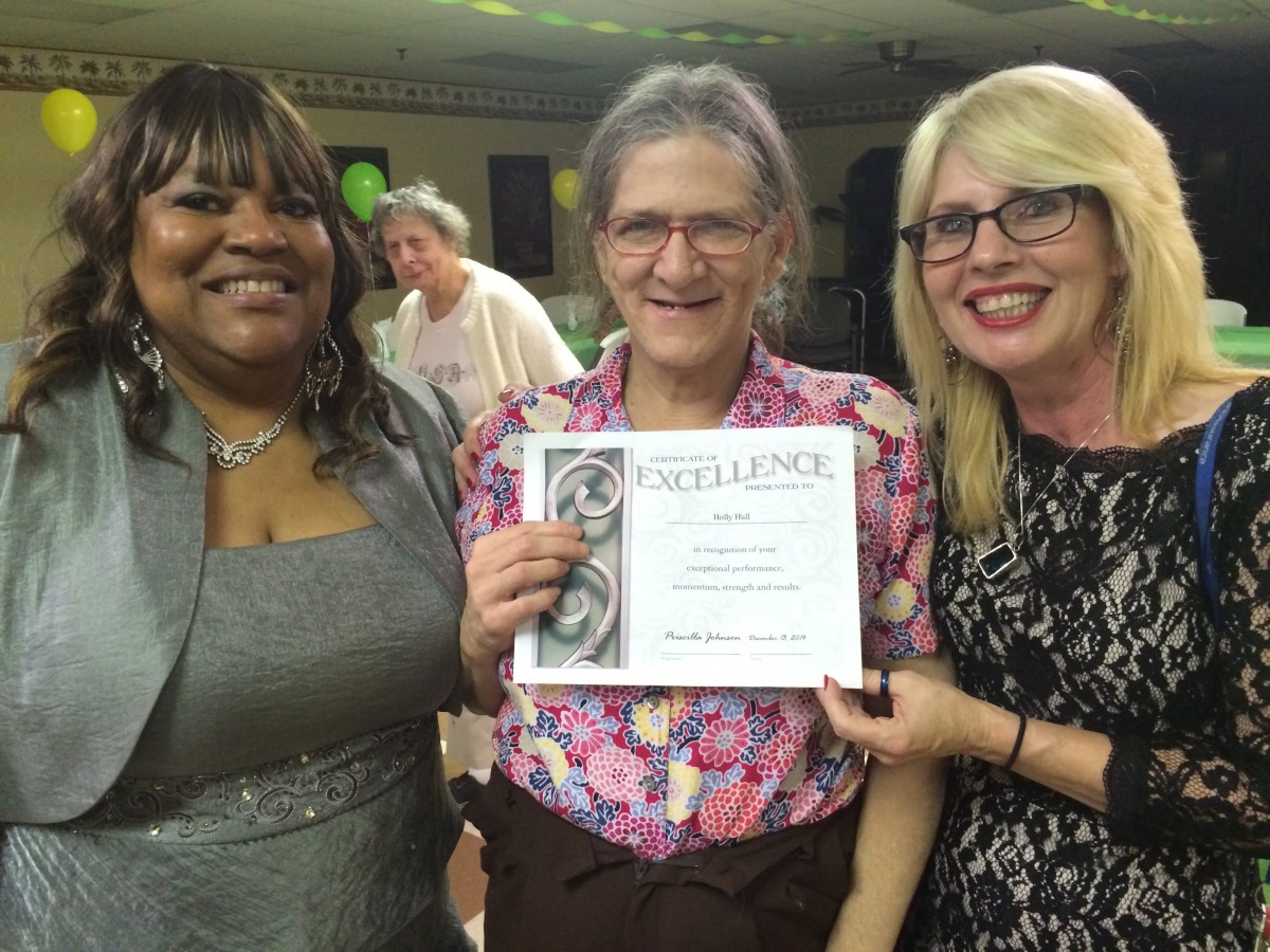 Three people smiling as one holds up a certificate of recognition.