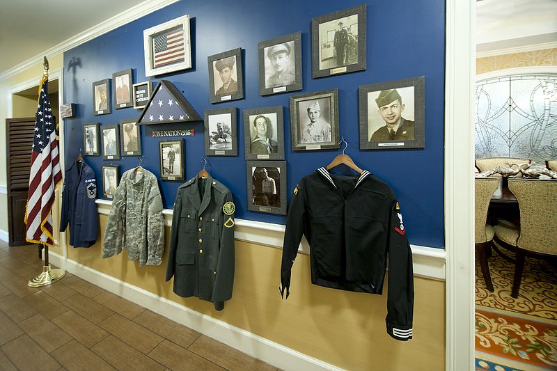 A wall display featuring framed photographs and military uniforms honoring veterans.