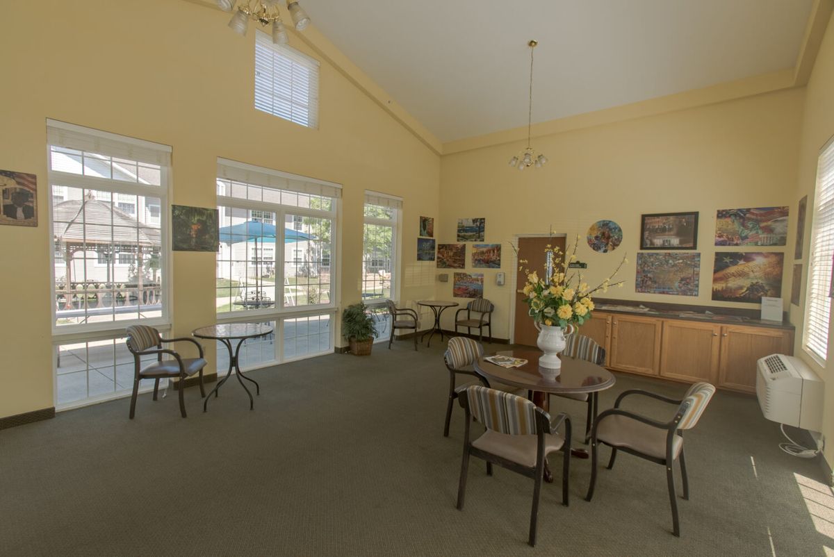 A spacious community room with tables and chairs, featuring large windows and decorative elements.