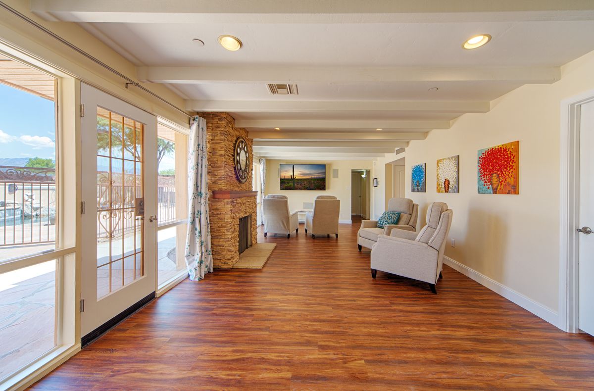 A spacious living room with hardwood floors, featuring a cozy fireplace and comfortable armchairs alongside large windows and colorful artwork.