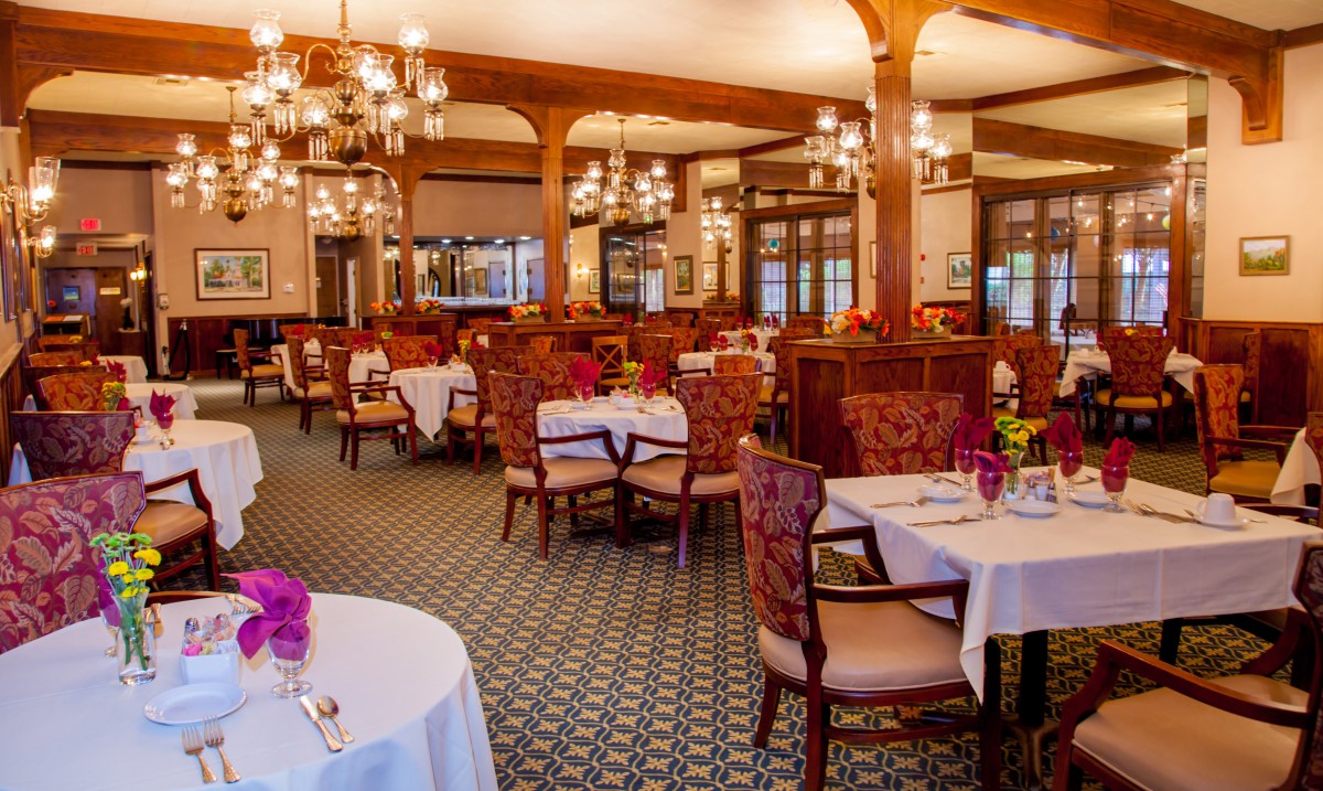 An elegant restaurant dining room with beautifully set tables and ornate chandeliers.