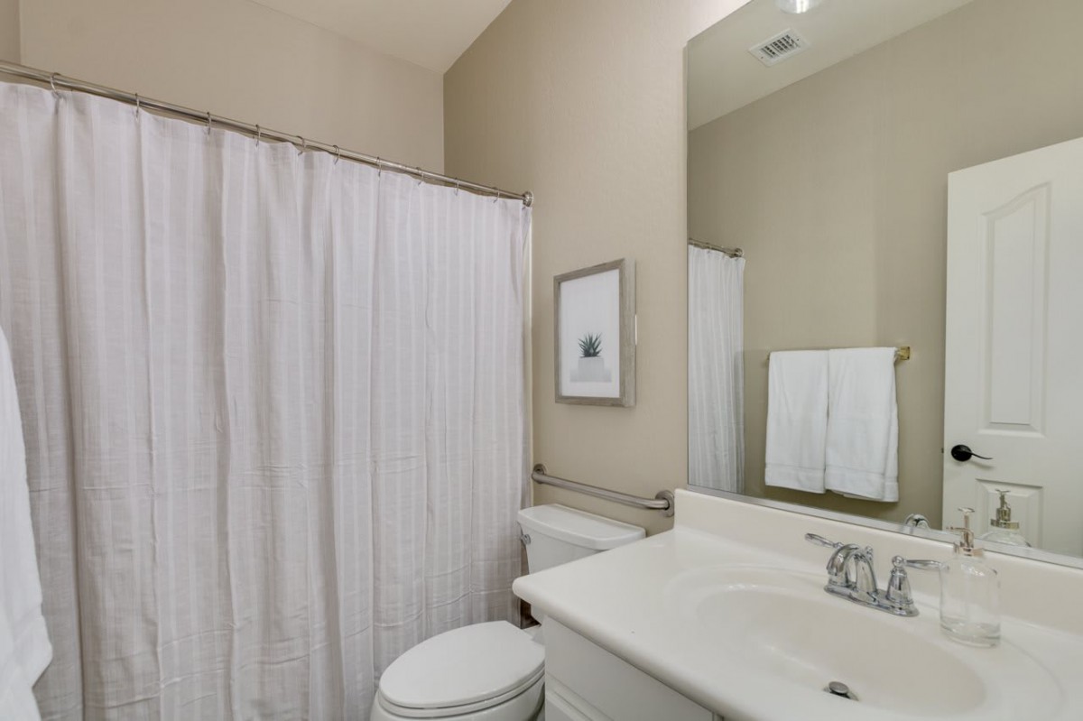 A modern bathroom with a sink, toilet, and shower curtain in neutral tones.