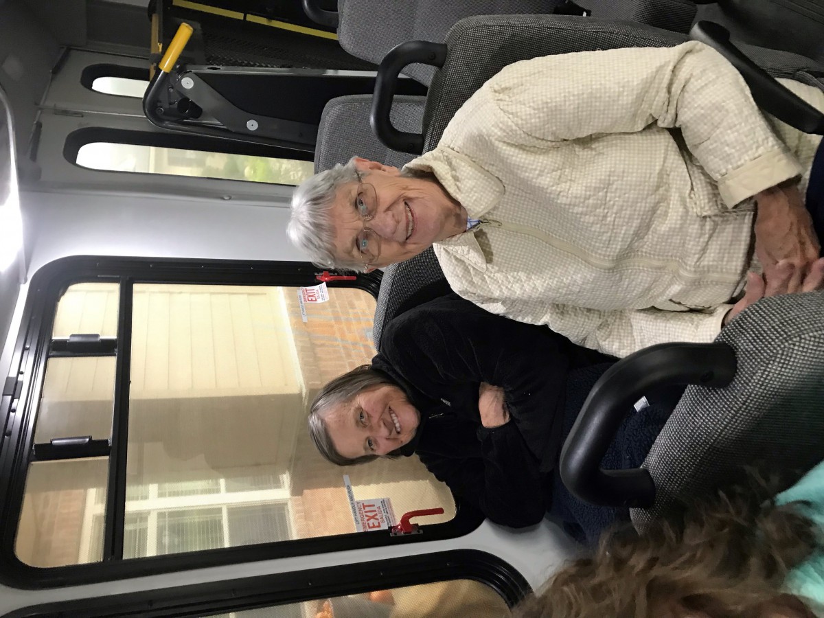 Two seniors enjoy a bus ride, smiling and seated comfortably.